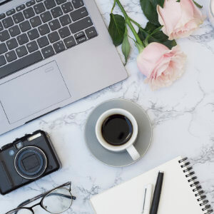 A laptop, camera and cup of coffee on a table.